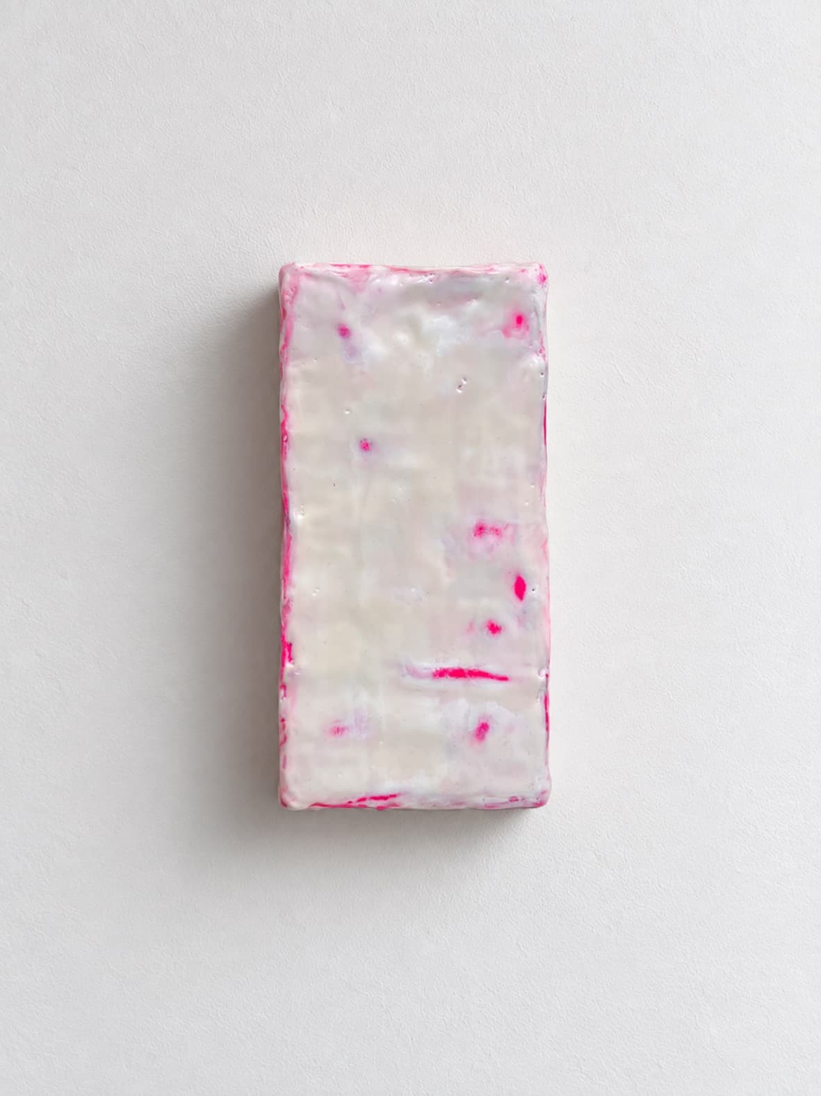 A waxed white brick with pink running along its edges, mounted upright on a white wall