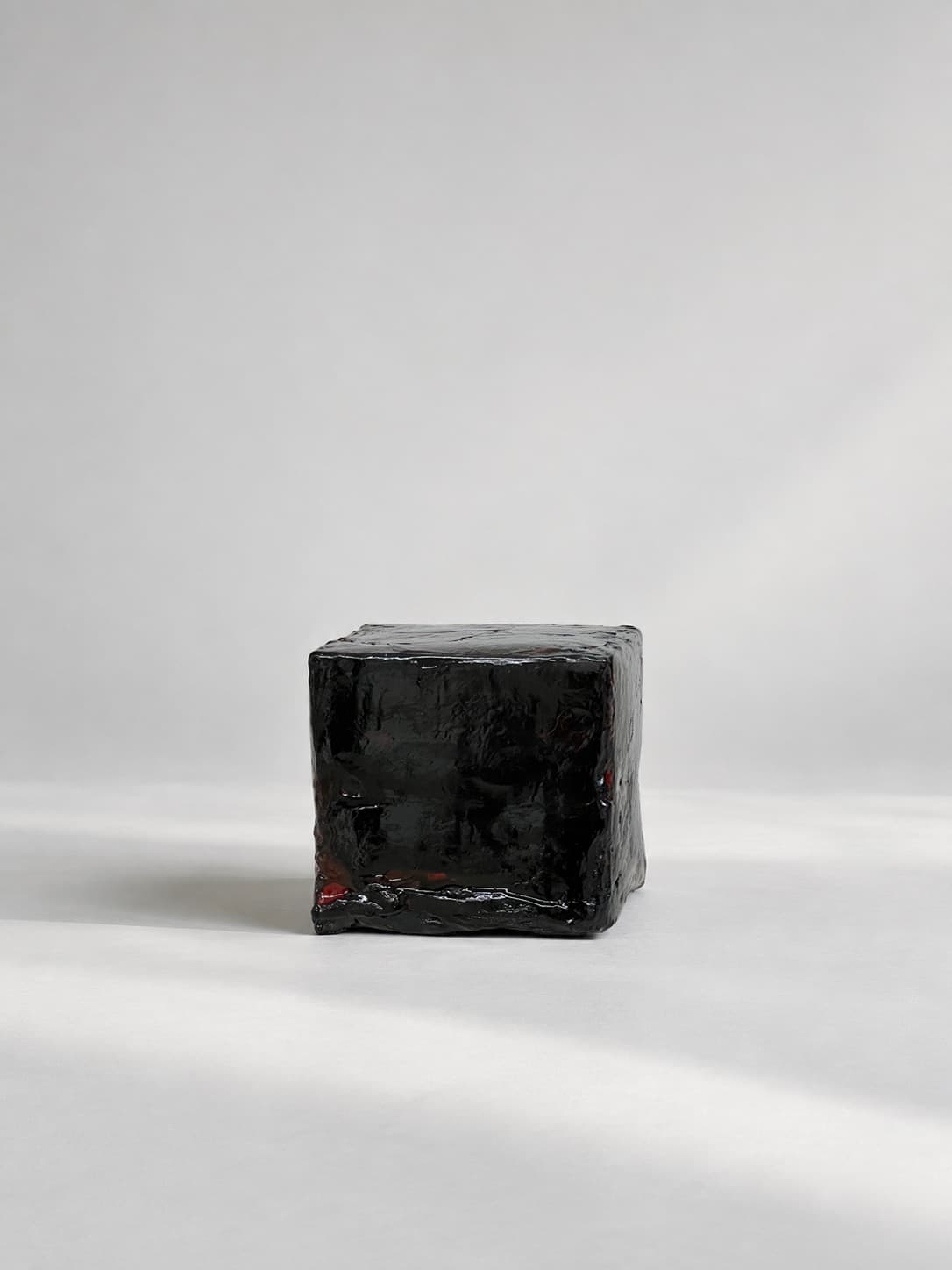 A black cube of textile waste sealed in dark wax, standing on a pale ground