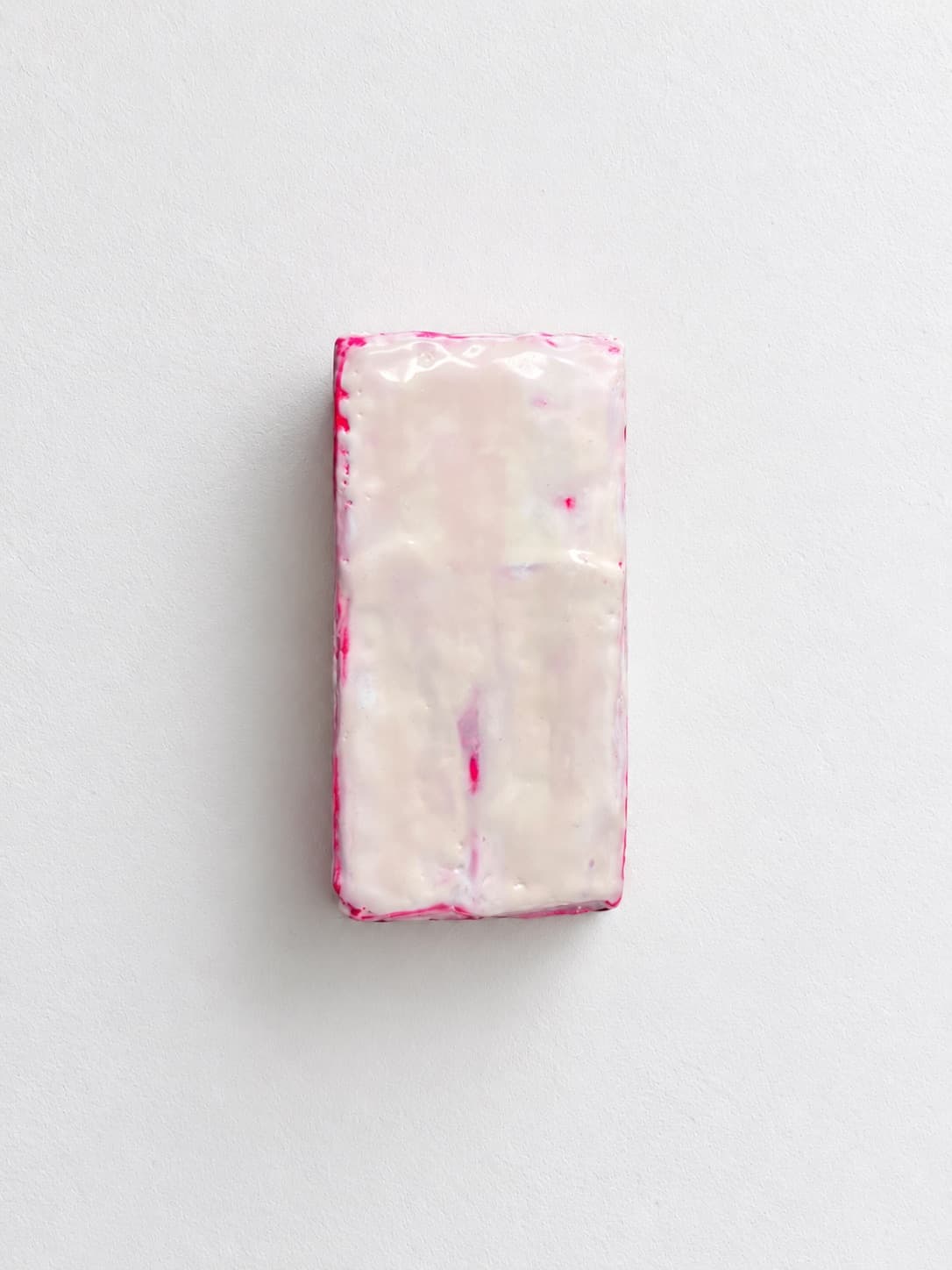 A waxed white brick edged in pink, mounted upright on a white wall