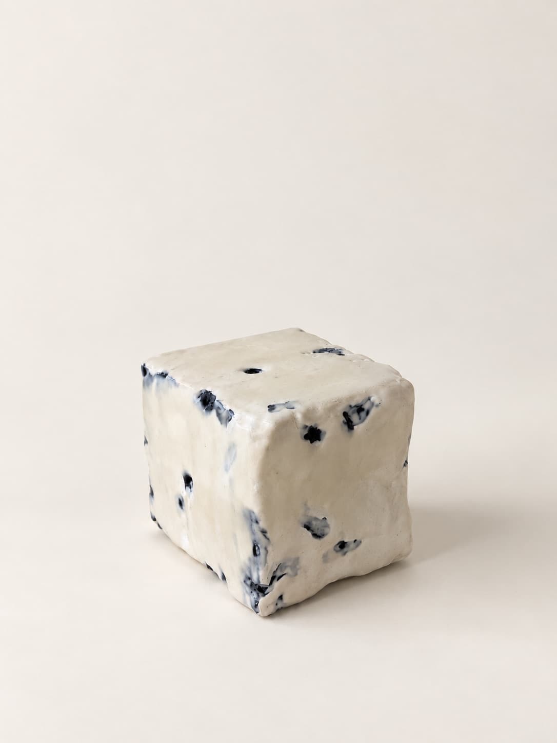A white cube of textile waste flecked with blue, standing on a pale ground