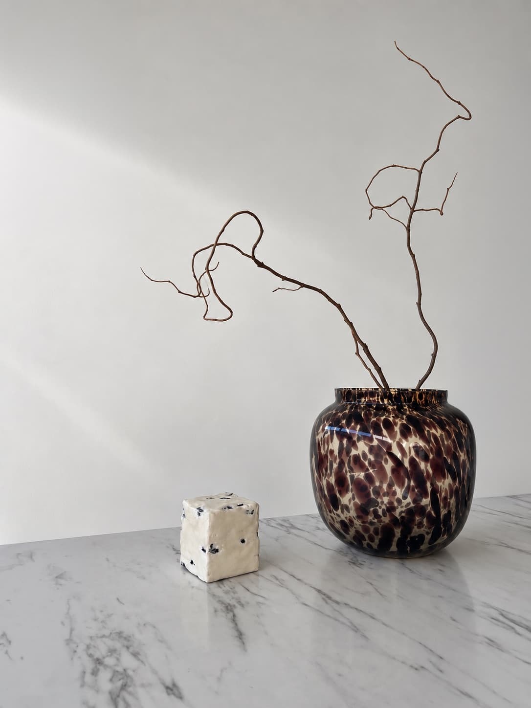 The cube on a marble surface beside a glass vase holding bare branches