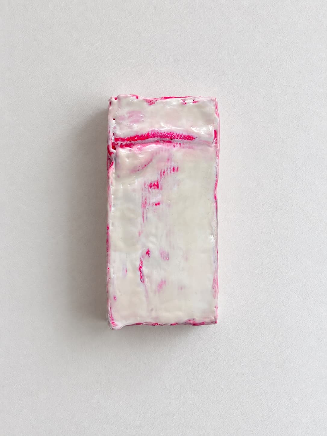 A waxed white brick crossed by a single pink seam, mounted upright on a white wall