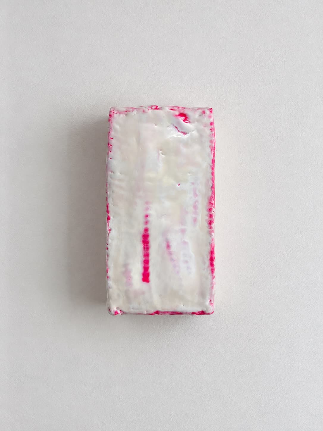 The object square to the wall, pink bleeding through the white wax