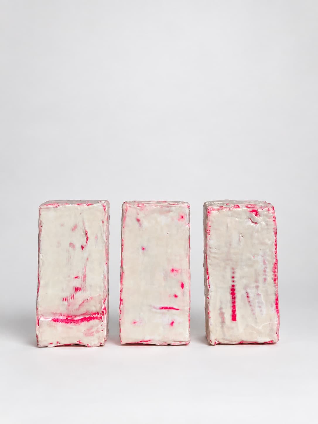 Three waxed bricks standing side by side on a pale ground