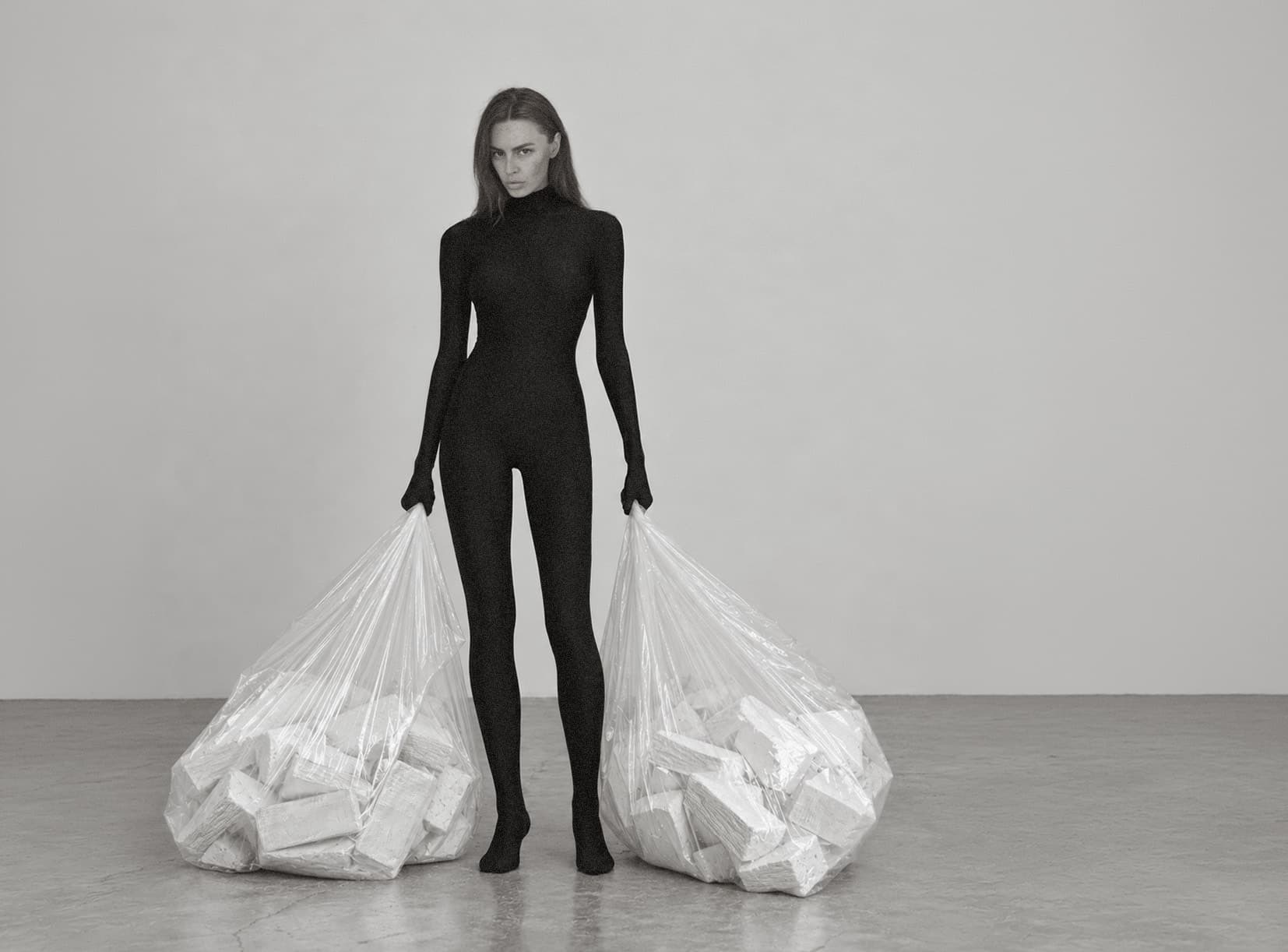 A figure in black standing between two clear sacks of white textile bricks