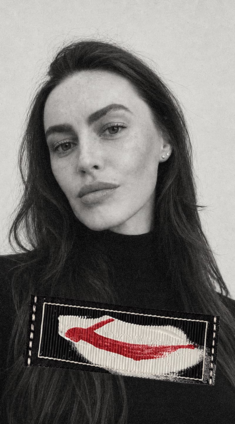 Olga Leonova in a black sweater, the artist's red painted mark stitched across the chest