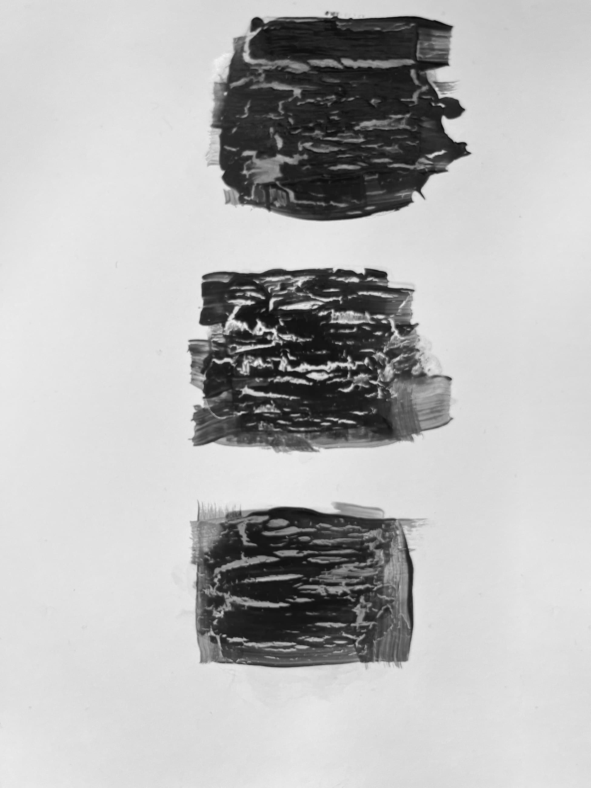 Three black brushed marks on white paper, one above the other