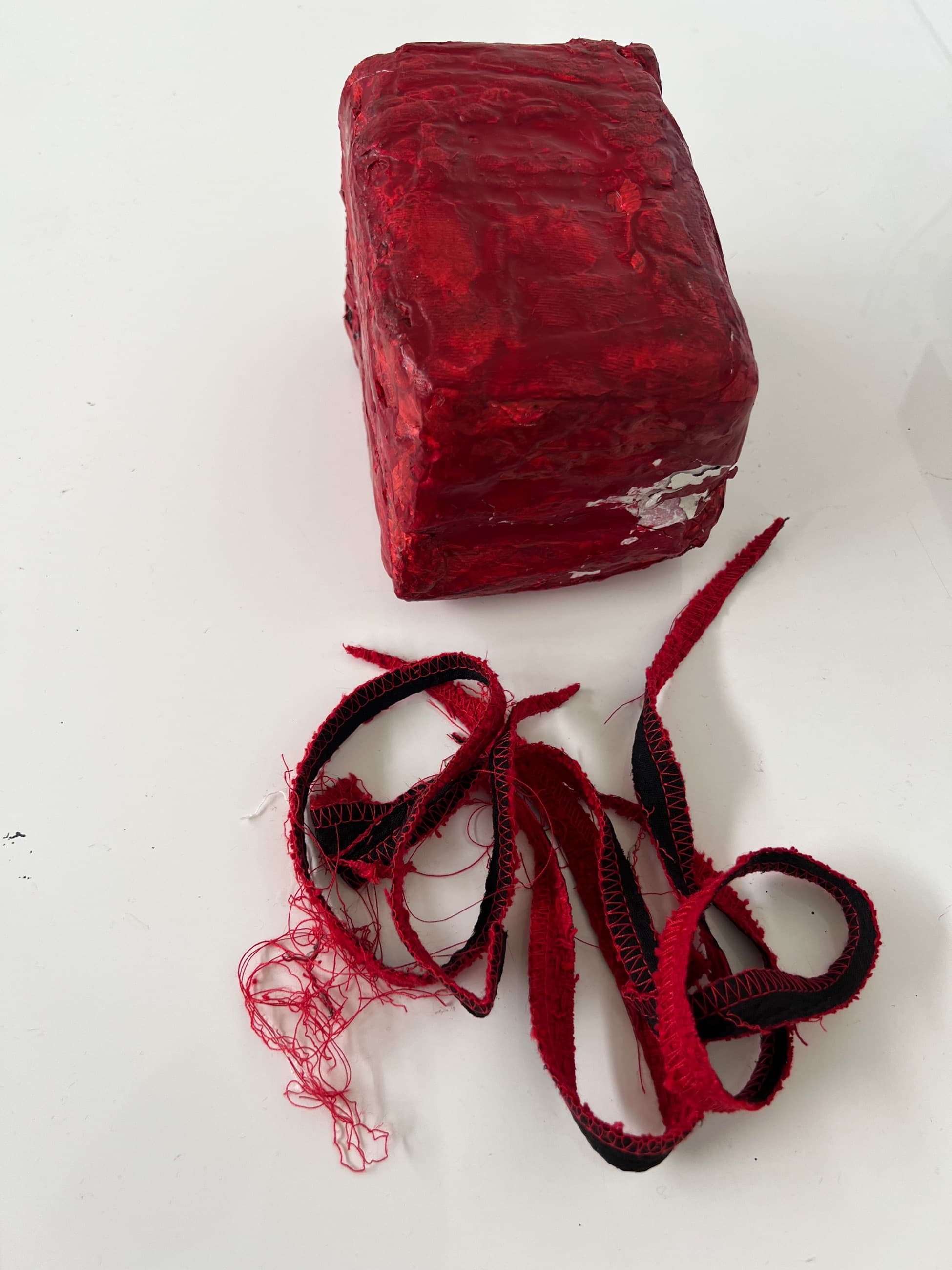 A red waxed brick on a white ground, loose red threads unwound beside it